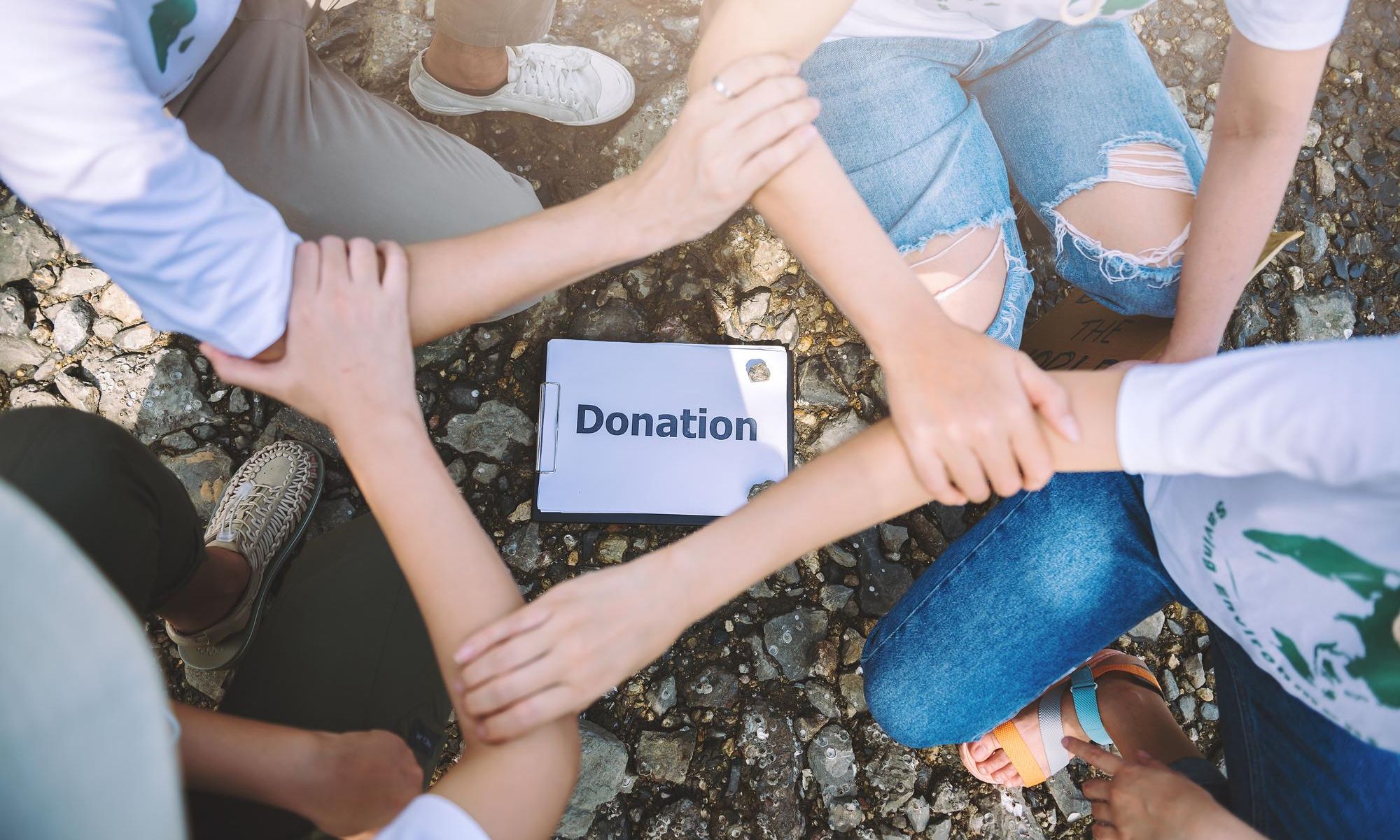 4 people holding hands in a circle and donation written on a paper at the center