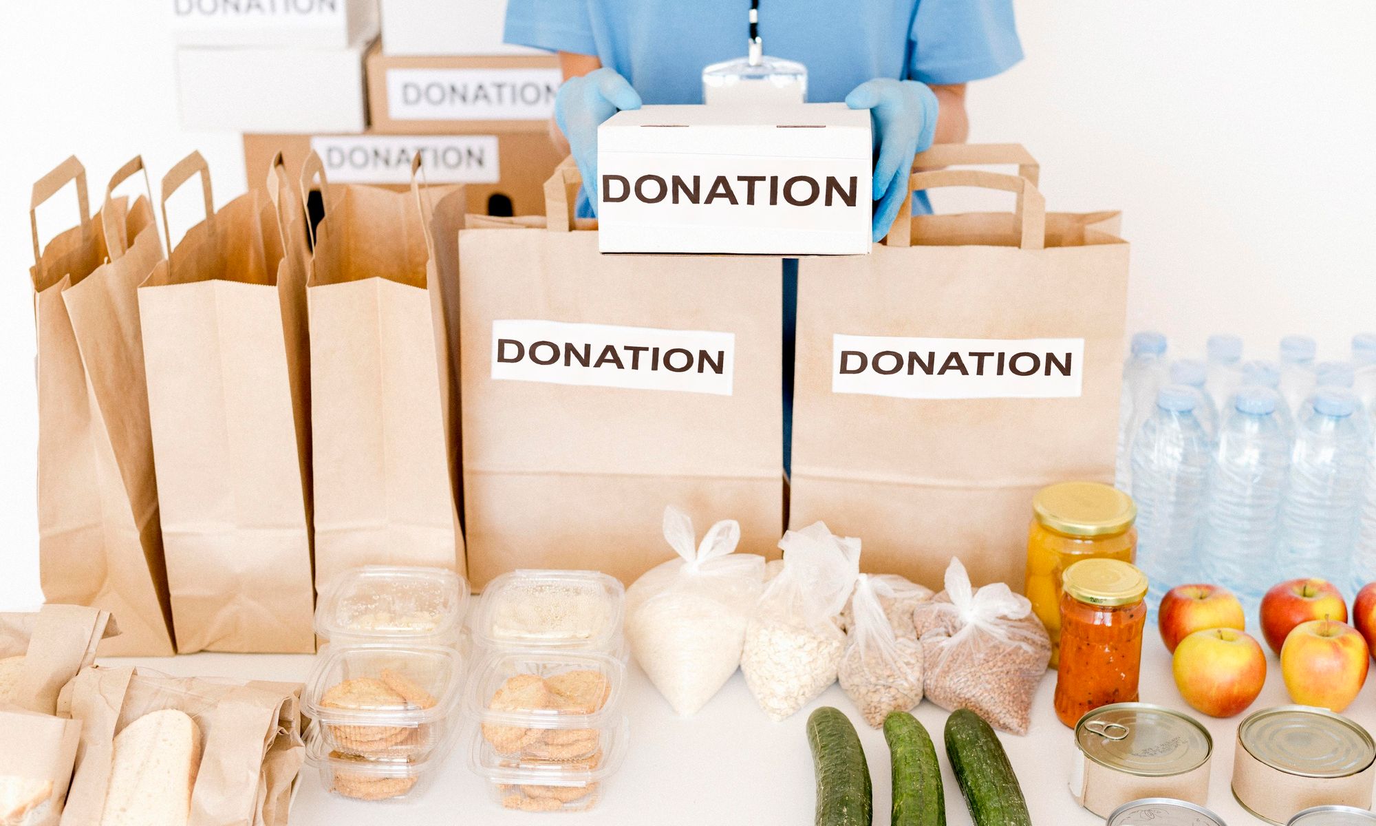 Many carry bags with Donation written on it placed on a table with many food items and water bottles